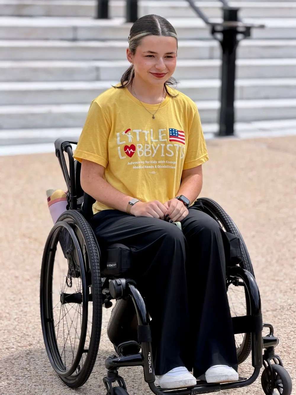Grace, a smiling woman in a yellow Little Lobbyists tee, seated in her wheelchair at the Capitol